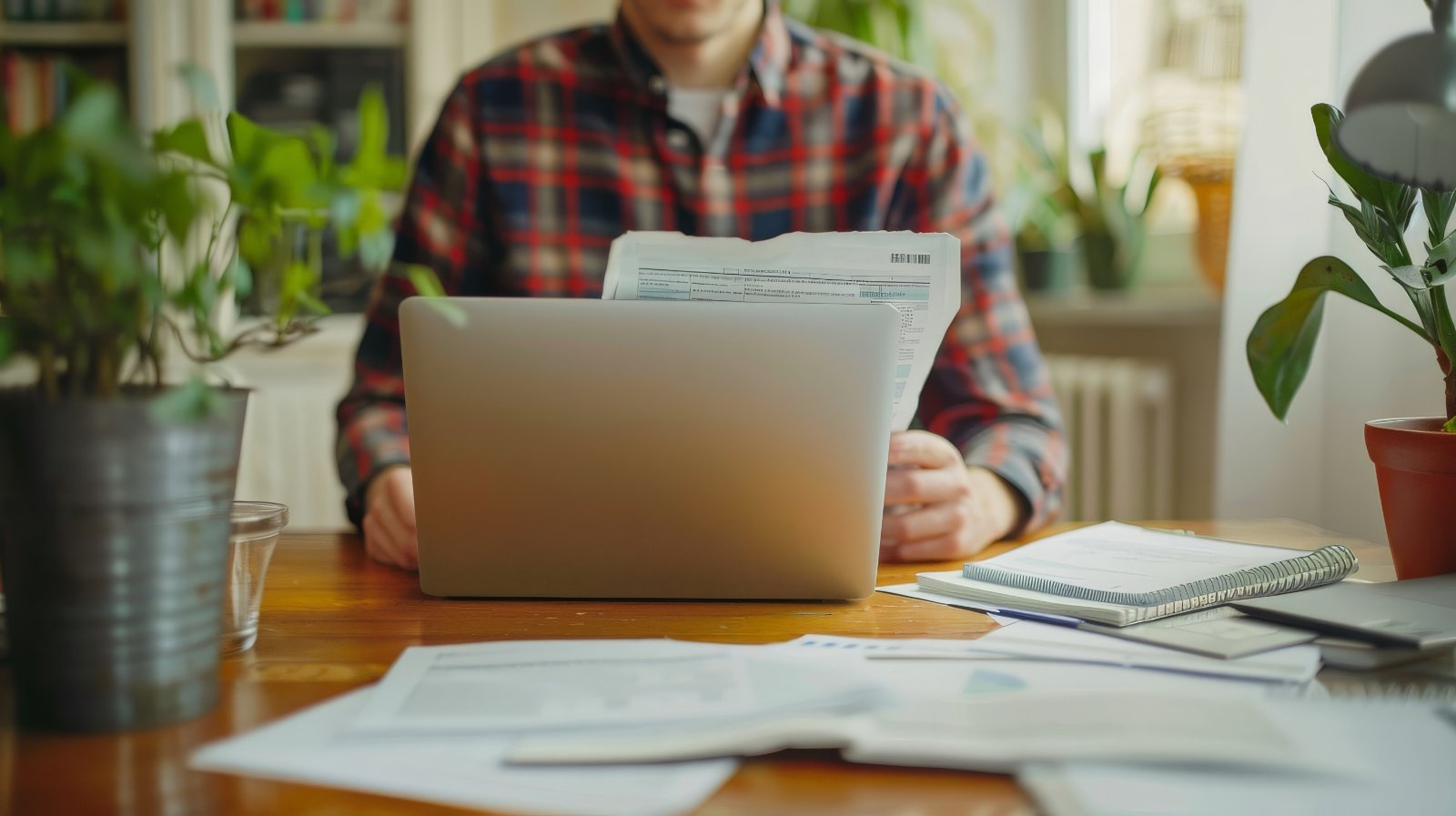 Scrivania con computer e documenti Uomo seduto alla scrivania lavora al computer portatile tra fogli e documenti sparsi sul piano