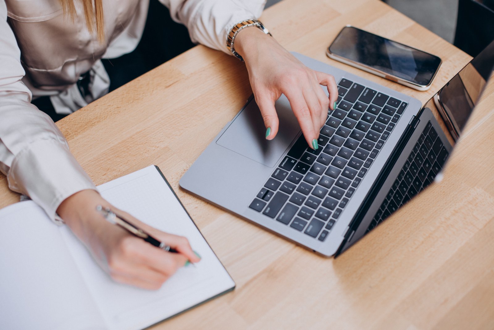 Appunti a mano accanto al portatile Mani che scrivono su un blocco per appunti accanto a un computer portatile e a uno smartphone