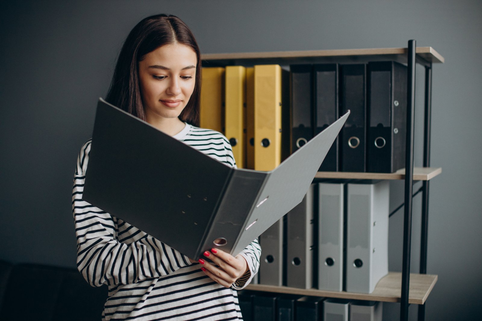 Consultazione di faldoni in archivio Donna in piedi davanti a uno scaffale di raccoglitori sfoglia un faldone di documenti