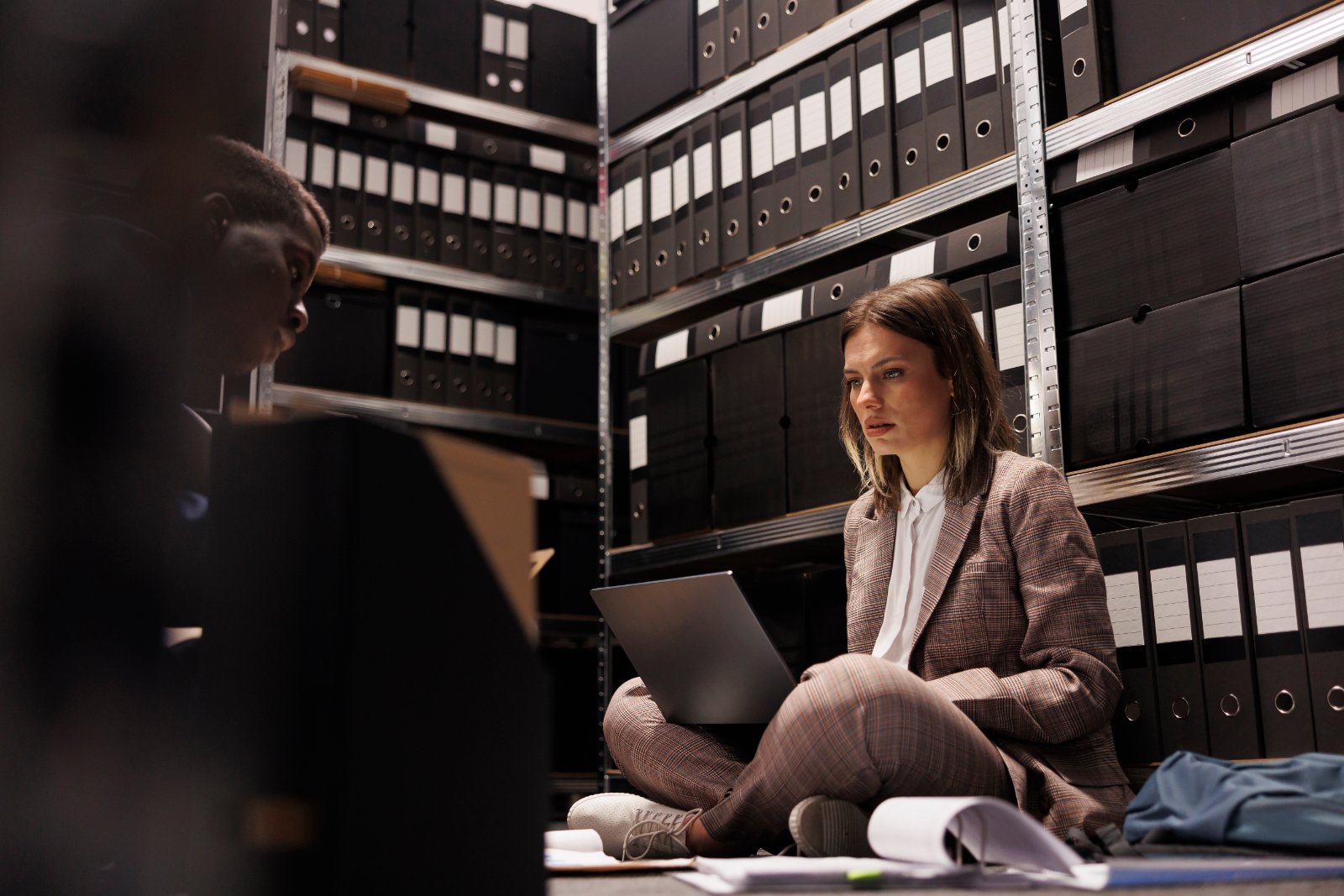 Archivio documentale Due persone consultano documenti in un archivio con scaffalature di scatole e faldoni